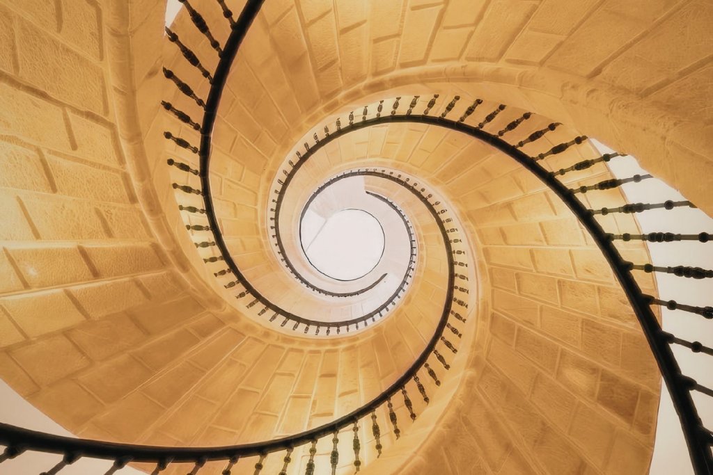 Vue du dessus d’un escalier en colimaçon en bois formant une spirale lumineuse et harmonieuse.
