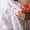 Femme tenant une fleur rouge dans une ambiance douce et intime, symbolisant les émotions retenues et la tension intérieure.