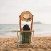 Femme assise face à la mer sur une plage, dans un fauteuil en bois, au coucher du soleil.