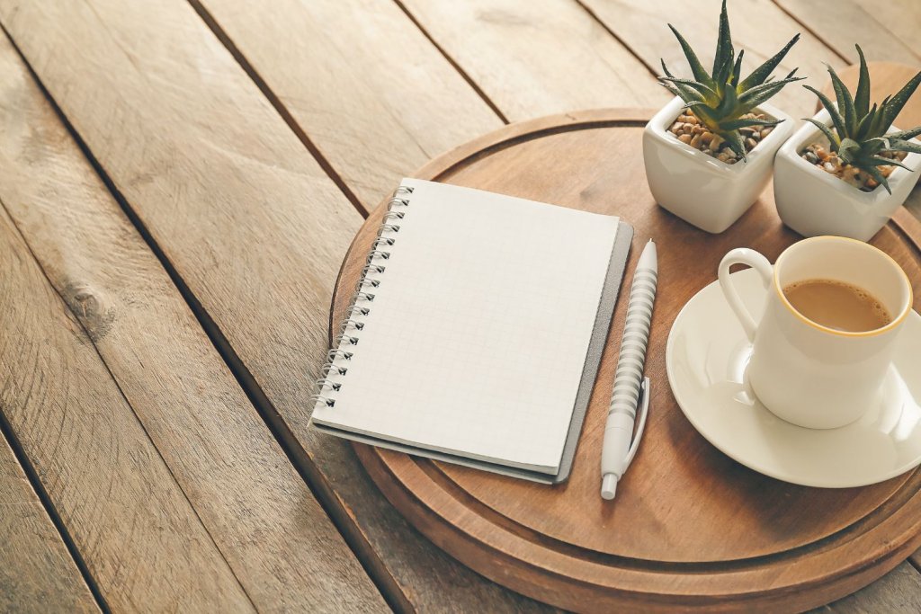 Carnet ouvert, stylo et tasse de café sur une table en bois, évoquant la planification et le besoin de ralentir.